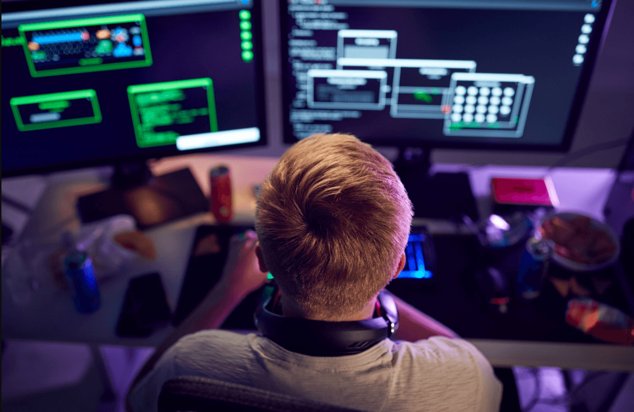 Jovem programador trabalhando em múltiplos monitores..png