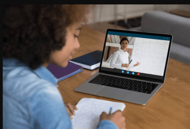 estudante olhando para o notebook e fazendo anotações