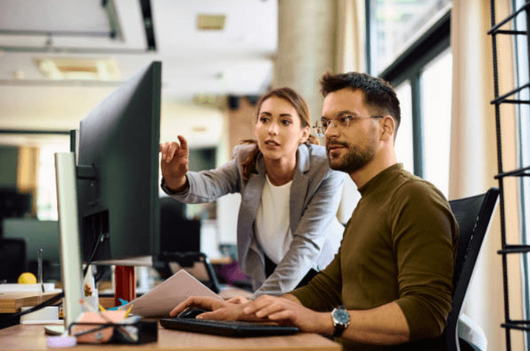 Dois colegas de trabalho analisando informações em um computador no escritório.png